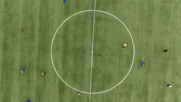 Aerial view of soccer players in yellow and blue jerseys competing on a green turf field with a white center circle in Lagos Lagos Nigeria. Aerial view of soccer players in yellow and blue jerseys competing on a green turf field with a white center circle in Lagos Lagos Nigeria.