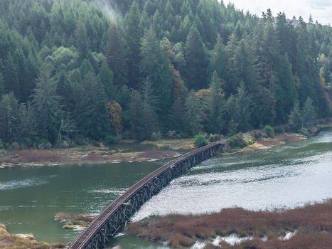 Aerial view of the Coos Bay Rail Line curving across wetlands beside the Siuslaw River near Florence Oregon with coastal rail infrastructure surrounded by forest and tidal marsh.