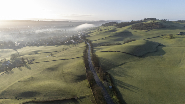 Aerial view of a road cutting through rolling green hills under a soft hazy morning light England United Kingdom. Aerial view of a road cutting through rolling green hills under a soft hazy morning light England United Kingdom.