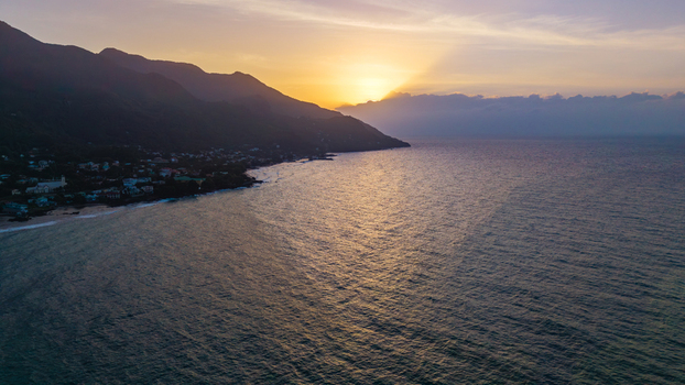 Aerial view of Anse Soleil Beachcomber Hotel along the coastline of Mahe at sunset with calm ocean waters lush hills and golden light. Mahe Baie Lazare Seychelles.