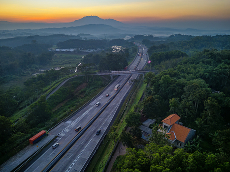 Aerial view of the Jalan Tol Bawen Salatiga highway winding through lush green hills and forests at sunset with distant mountains in Tengaran Central Java Indonesia. Aerial view of the Jalan Tol Bawen Salatiga highway winding through lush green hills and forests at sunset with distant mountains in Tengaran Central Java Indonesia.