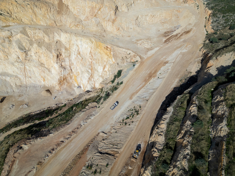 Aerial view of an open pit quarry with heavy machinery operating on dirt paths surrounded by steep rocky cliffs in Teulada Valencian Community Spain.