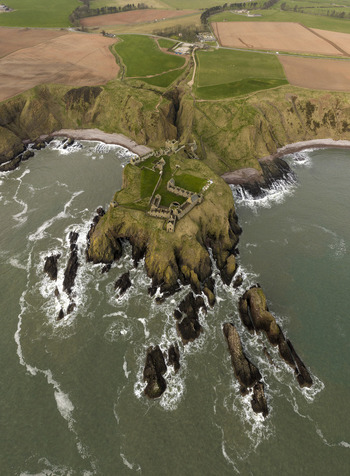 Aerial view of Dunnottar Castle ruins on a dramatic rocky cliff surrounded by the North Sea and green coastal fields Stonehaven Scotland United Kingdom. Aerial view of Dunnottar Castle ruins on a dramatic rocky cliff surrounded by the North Sea and green coastal fields Stonehaven Scotland United Kingdom.