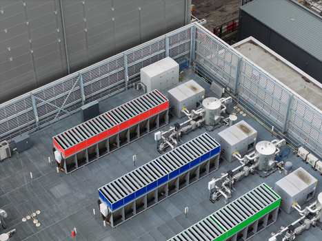 Aerial view of a data center rooftop featuring industrial cooling units with red blue and green accents complex piping systems and HVAC equipment in the United Kingdom.