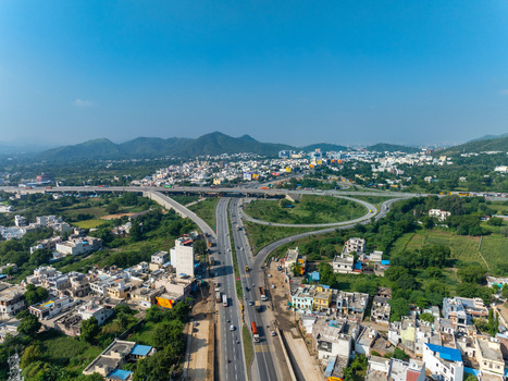 Aerial view of a highway interchange surrounded by urban buildings green fields and distant hills in Udaipur Rajasthan India. Aerial view of a highway interchange surrounded by urban buildings green fields and distant hills in Udaipur Rajasthan India.