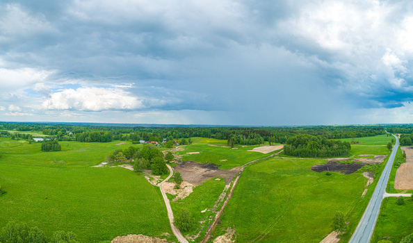 Aerial view of lush green fields patches of forest and a winding road under a dramatic cloudy sky in Latvia. Aerial view of lush green fields patches of forest and a winding road under a dramatic cloudy sky in Latvia.
