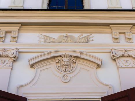 View of the ornate architectural details of Belvedere Palace featuring a grotesque mask relief and military trophy carvings on the white facade in Vienna Vienna Austria. View of the ornate architectural details of Belvedere Palace featuring a grotesque mask relief and military trophy carvings on the white facade in Vienna Vienna Austria.