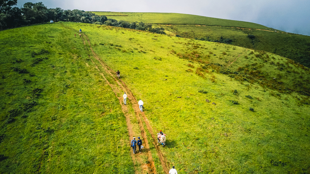 Aerial view of hikers traversing a verdant green hillside on a narrow trail under a soft diffused light Obudu Cross River Nigeria.