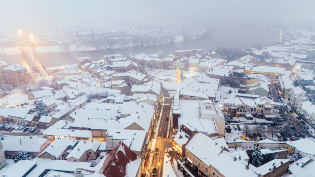 Aerial view of the snow covered town center featuring historic rooftops a bridge over the Sava River and illuminated streets in Sremska Mitrovica Vojvodina Serbia.