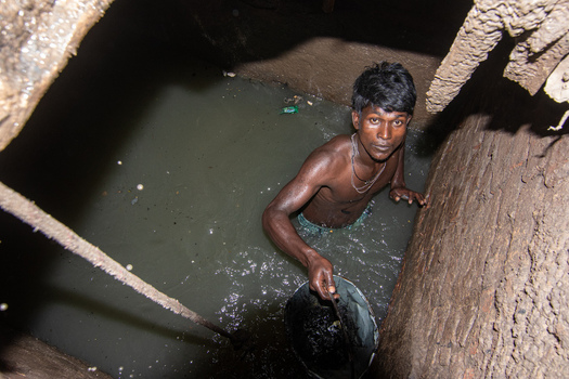 Dhaka Bangladesh 18 April 2018 View of a man working inside a dark sewer manhole standing in murky water while holding a bucket in a confined underground space. Dhaka Bangladesh 18 April 2018 View of a man working inside a dark sewer manhole standing in murky water while holding a bucket in a confined underground space.