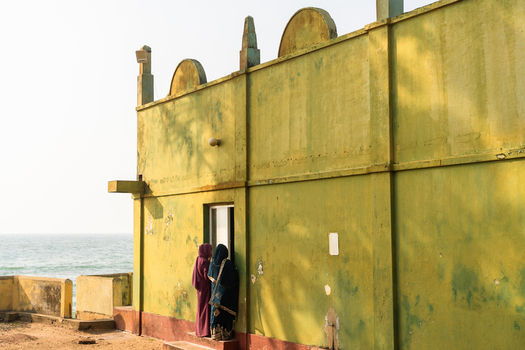 View of two women in traditional dress standing by a weathered yellow building overlooking the sea in Galle Southern Province Sri Lanka.