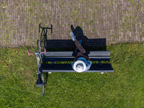 Aerial view of a person relaxing on a bench beside a bicycle contrasting the green grass and textured paving stones Palendijk Utrecht Netherlands.