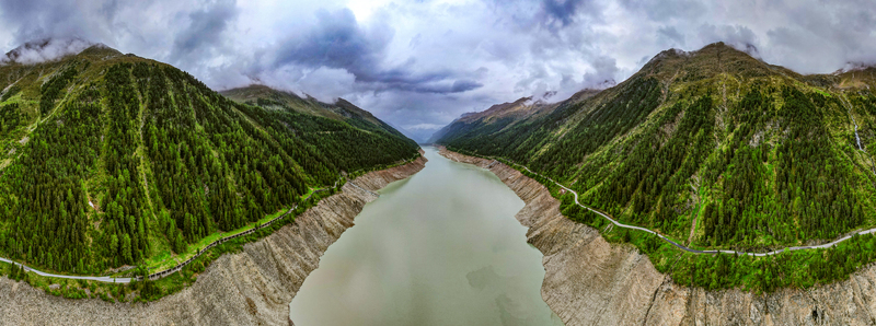Aerial view of the Gepatsch Reservoir surrounded by steep pine covered mountain slopes rocky banks and a winding road under a cloudy sky in Prutz Tyrol Austria. Aerial view of the Gepatsch Reservoir surrounded by steep pine covered mountain slopes rocky banks and a winding road under a cloudy sky in Prutz Tyrol Austria.