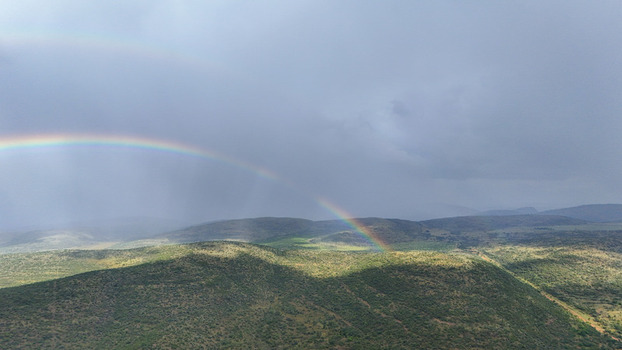 Aerial view of a vibrant double rainbow arching over the rolling green hills and rugged terrain under a dramatic stormy sky in the Waterberg District Municipality Limpopo South Africa. Aerial view of a vibrant double rainbow arching over the rolling green hills and rugged terrain under a dramatic stormy sky in the Waterberg District Municipality Limpopo South Africa.