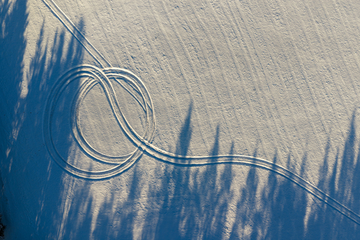 Aerial view of vehicle tracks forming circular patterns on a snow covered field with long tree shadows in winter light Lithuania. Aerial view of vehicle tracks forming circular patterns on a snow covered field with long tree shadows in winter light Lithuania.