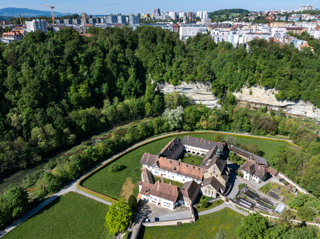 Aerial view of the historic La Maigrauge abbey complex nestled among lush green forests and the Sarine river with the city skyline in the background in Fribourg Fribourg Switzerland. Aerial view of the historic La Maigrauge abbey complex nestled among lush green forests and the Sarine river with the city skyline in the background in Fribourg Fribourg Switzerland.
