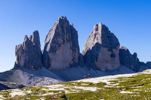 View of Tre Cime di Lavaredo with hikers walking on a rocky trail under a clear blue sky in Auronzo di Cadore Veneto Italy.