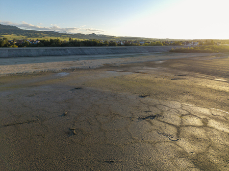 Aerial view of a dried up reservoir bed with cracked mud patterns distant dam and rolling hills under golden hour light in Czorsztyn Lesser Poland Voivode Poland. Aerial view of a dried up reservoir bed with cracked mud patterns distant dam and rolling hills under golden hour light in Czorsztyn Lesser Poland Voivode Poland.