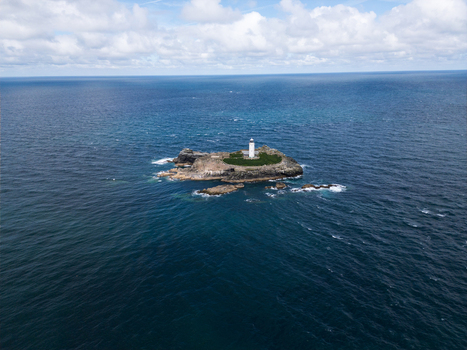 Aerial view of Godrevy Lighthouse on a small rocky island surrounded by the deep blue waters of the Atlantic Ocean under a cloudy sky in Gwithian England United Kingdom. Aerial view of Godrevy Lighthouse on a small rocky island surrounded by the deep blue waters of the Atlantic Ocean under a cloudy sky in Gwithian England United Kingdom.