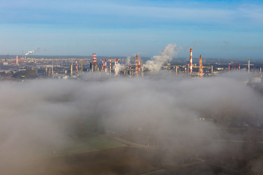 Aerial view of a sprawling refinery complex its chimneys piercing through a sea of fog under a pale blue sky Gdansk Pomorskie voivodeship Poland. Aerial view of a sprawling refinery complex its chimneys piercing through a sea of fog under a pale blue sky Gdansk Pomorskie voivodeship Poland.