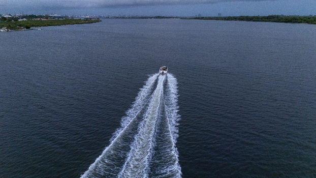 Aerial view of a motorboat cruising across the calm waters of the lagoon with a white wake and lush green shorelines under a cloudy sky in Badagry Lagos Nigeria. Aerial view of a motorboat cruising across the calm waters of the lagoon with a white wake and lush green shorelines under a cloudy sky in Badagry Lagos Nigeria.