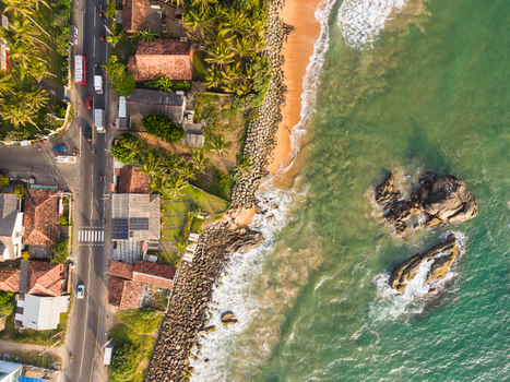 Aerial view of the coastline featuring a road with traffic palm trees and turquoise waves crashing against a sandy beach in Galle Southern Province Sri Lanka.
