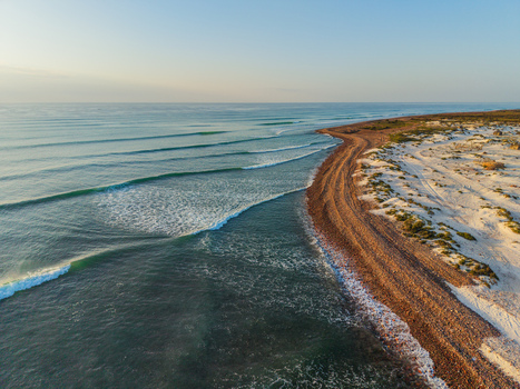 Aerial view of the shoreline where the turquoise waves gently meet the reddish brown sandy beach contrasting against the clear blue sky Kadrihnitin Yemen. Aerial view of the shoreline where the turquoise waves gently meet the reddish brown sandy beach contrasting against the clear blue sky Kadrihnitin Yemen.