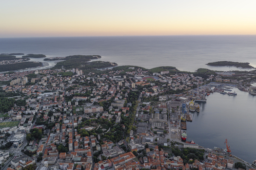Aerial view of the coastal city of Pula with its historic harbor industrial shipyard cranes and dense residential rooftops overlooking the Adriatic Sea in Pula Istarska zupanija Croatia. Aerial view of the coastal city of Pula with its historic harbor industrial shipyard cranes and dense residential rooftops overlooking the Adriatic Sea in Pula Istarska zupanija Croatia.