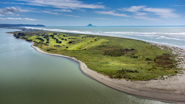 Aerial view of the Ohope Golf Club situated on a coastal spit with green fairways sand dunes and the Pacific Ocean under a blue sky in Ohope Bay of Plenty Region New Zealand.