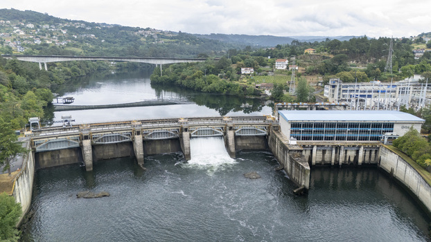 Aerial view of Subestacion Electrica Velle and the Velle Dam on the Minho River with water flowing through the spillway and lush green hills in the background Ourense Ourense Spain.