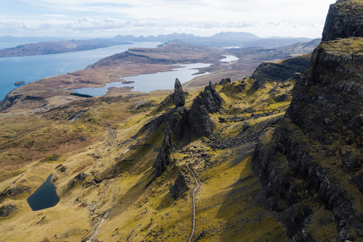 Aerial view of The Storr a dramatic rocky landscape with jagged cliffs and grassy slopes overlooking the sea and distant lochs in Portree Scotland United Kingdom. Aerial view of The Storr a dramatic rocky landscape with jagged cliffs and grassy slopes overlooking the sea and distant lochs in Portree Scotland United Kingdom.
