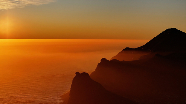 Aerial view of rugged mountain peaks silhouetted against a vibrant orange sunset over the Atlantic Ocean with low mist in the valleys in Cape Town Western Cape South Africa. Aerial view of rugged mountain peaks silhouetted against a vibrant orange sunset over the Atlantic Ocean with low mist in the valleys in Cape Town Western Cape South Africa.