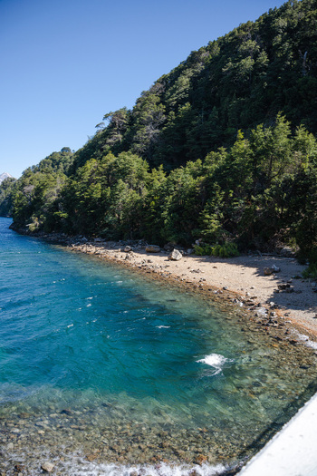 View of the Puente Arroyo La Angostura railing overlooking the clear blue waters of Nahuel Huapi Lake and the forested shoreline in San Carlos de Bariloche Rio Negro Argentina.