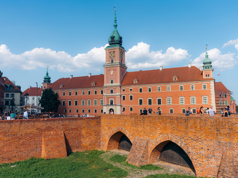 View of the Royal Castle in Warsaw with its distinctive orange facade and clock tower rising above the historic brick fortifications of the Old Town in Warsaw Masovian Voivodeship Poland. View of the Royal Castle in Warsaw with its distinctive orange facade and clock tower rising above the historic brick fortifications of the Old Town in Warsaw Masovian Voivodeship Poland.