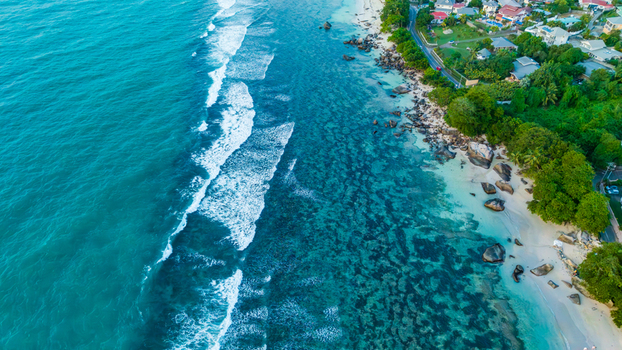 Aerial view of Beau Vallon Beach with turquoise waters crashing waves scattered rocks and lush coastal vegetation in Beau Vallon Seychelles.