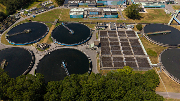 Aerial view of a wastewater treatment plant with large circular sedimentation tanks and rectangular aeration basins surrounded by trees and industrial buildings in Milan Lombardy Italy. Aerial view of a wastewater treatment plant with large circular sedimentation tanks and rectangular aeration basins surrounded by trees and industrial buildings in Milan Lombardy Italy.