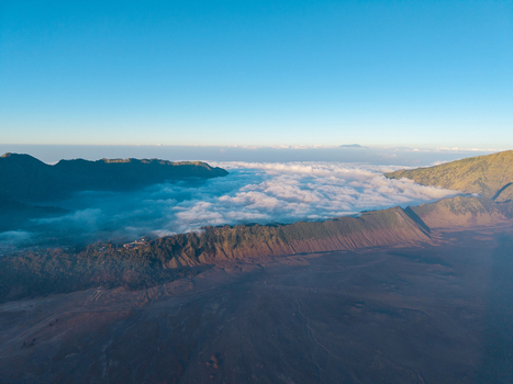 Aerial view of Mount Bromo with volcanic terrain and a sea of clouds under a clear blue sky in Tosari East Java Indonesia.