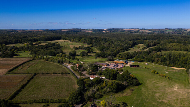 Aerial view of Hamptworth Golf course featuring lush green fairways surrounding dense woodland the clubhouse and a parking area under a clear blue sky in Hamptworth England United Kingdom. Aerial view of Hamptworth Golf course featuring lush green fairways surrounding dense woodland the clubhouse and a parking area under a clear blue sky in Hamptworth England United Kingdom.