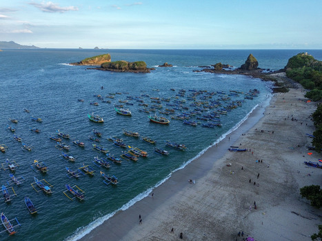 Aerial view of Papuma Beach with numerous traditional fishing boats anchored in the blue sea sandy coastline and rocky outcrops in Jember East Java Indonesia. Aerial view of Papuma Beach with numerous traditional fishing boats anchored in the blue sea sandy coastline and rocky outcrops in Jember East Java Indonesia.