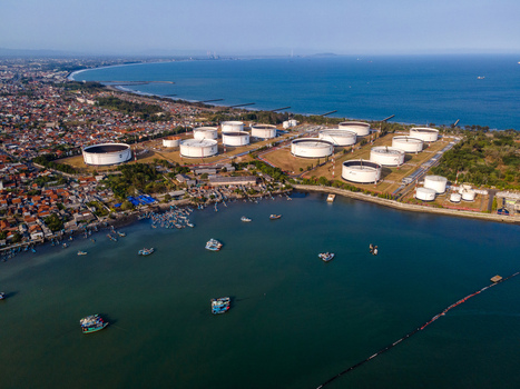 Aerial view of an oil storage terminal with large white cylindrical tanks situated along the coast near a fishing harbor with small boats in Cilacap Regency Central Java Indonesia. Aerial view of an oil storage terminal with large white cylindrical tanks situated along the coast near a fishing harbor with small boats in Cilacap Regency Central Java Indonesia.