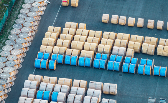 Aerial view of wooden and blue covered cable drums stored in organized rows at an industrial facility highlighting logistics manufacturing and electrical infrastructure. Italy. Aerial view of wooden and blue covered cable drums stored in organized rows at an industrial facility highlighting logistics manufacturing and electrical infrastructure. Italy.