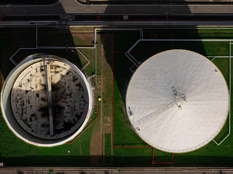 Aerial view of two large industrial storage tanks one white and one open surrounded by green grass and piping infrastructure in Bajos de Haina San Cristobal Province Dominican Republic.