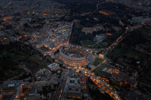 Roma Italy 06 April 2022 Aerial view of the illuminated Colosseum at night surrounded by the historic urban landscape of Rome with glowing street lights and ancient architecture. Roma Italy 06 April 2022 Aerial view of the illuminated Colosseum at night surrounded by the historic urban landscape of Rome with glowing street lights and ancient architecture.