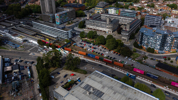 Aerial view of a freight train passing through an urban area with modern buildings parking lots and roads in Southampton England United Kingdom. Aerial view of a freight train passing through an urban area with modern buildings parking lots and roads in Southampton England United Kingdom.