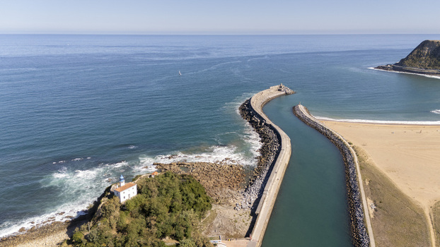 Aerial view of the San Telmo chapel and lighthouse on the rocky coast of Zumaia with a long breakwater sandy beach and clear blue water in Zumaia Basque Country Spain.