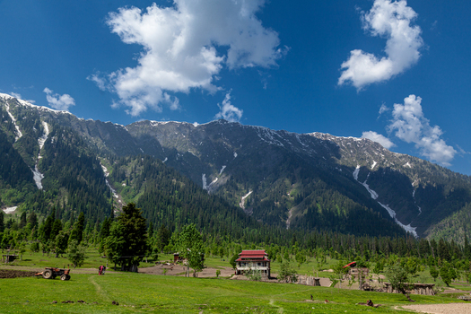 View of Arang Kel village in Neelum Valley with traditional wooden houses lush green meadows and snow capped mountains under a blue sky Arang Kel Azad Kashmir Pakistan. View of Arang Kel village in Neelum Valley with traditional wooden houses lush green meadows and snow capped mountains under a blue sky Arang Kel Azad Kashmir Pakistan.