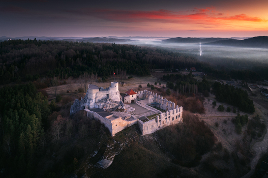 Aerial view of the medieval castle ruins on a rocky hill surrounded by dense forest and morning mist in Krakow County Lesser Poland Voivodeship Poland. Aerial view of the medieval castle ruins on a rocky hill surrounded by dense forest and morning mist in Krakow County Lesser Poland Voivodeship Poland.