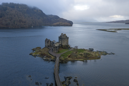 Aerial view of Eilean Donan Castle on its small tidal island connected by a stone bridge over Loch Duich under a misty sky Dornie Scotland United Kingdom.
