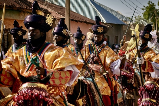 Zaria city Nigeria 21 March 2026 View of a majestic procession of horsemen adorned in shimmering golden robes and dark turbans parading vibrantly down a sun drenched street. Zaria city Nigeria 21 March 2026 View of a majestic procession of horsemen adorned in shimmering golden robes and dark turbans parading vibrantly down a sun drenched street.