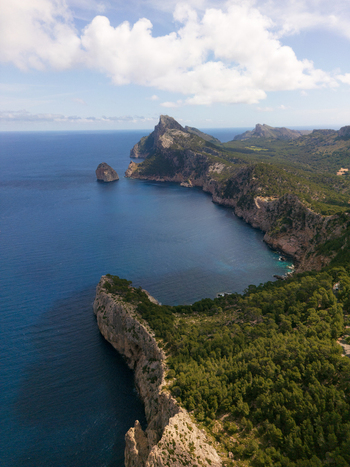 Aerial view of Cap de Formentor with dramatic limestone cliffs green pine forests and the blue Mediterranean Sea under a cloudy sky Balearic Islands Balearic Islands Spain.